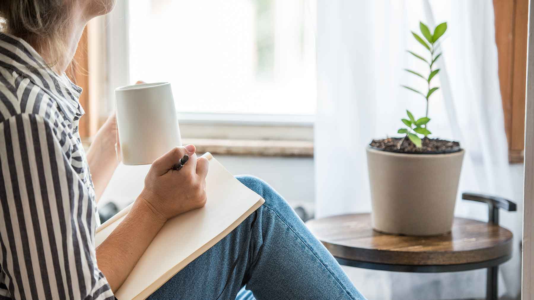 Person practicing morning wellness routine with journal and tea